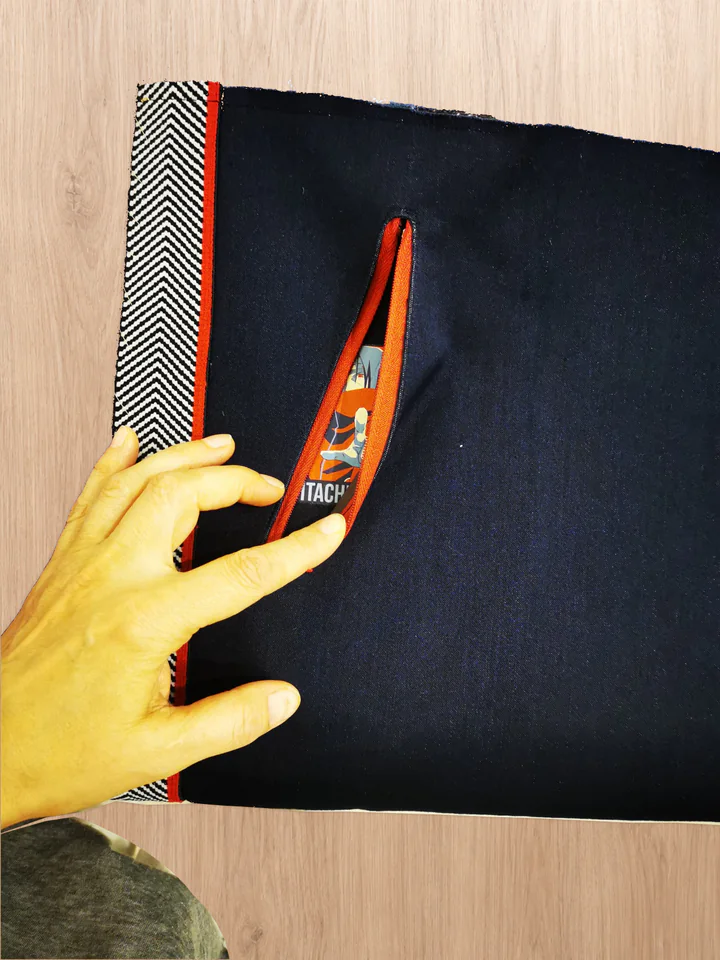An open red zipper reveals part of the iron-on graphic on the navy pocket backing; a hand holds the opening apart.