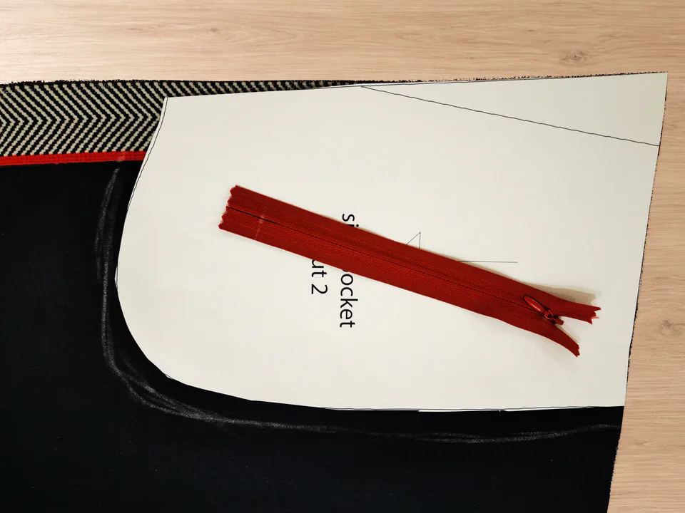 Paper pocket pattern piece and red zipper positioned on a navy trouser front.