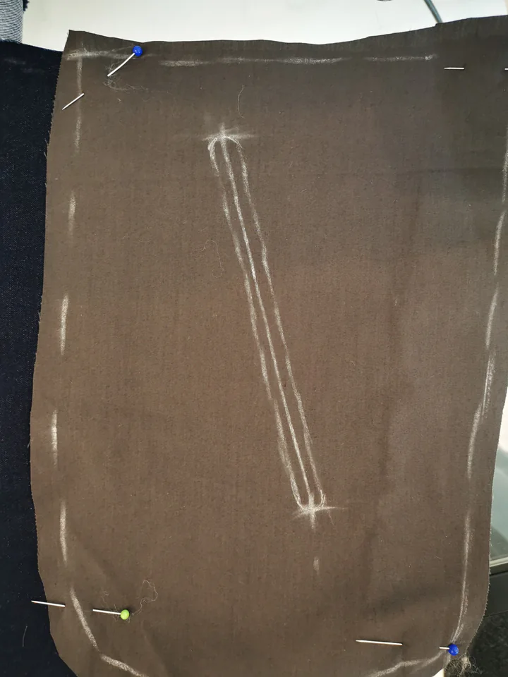 Brown lining pinned over a navy trouser front with a rounded slot and centre line marked in chalk.