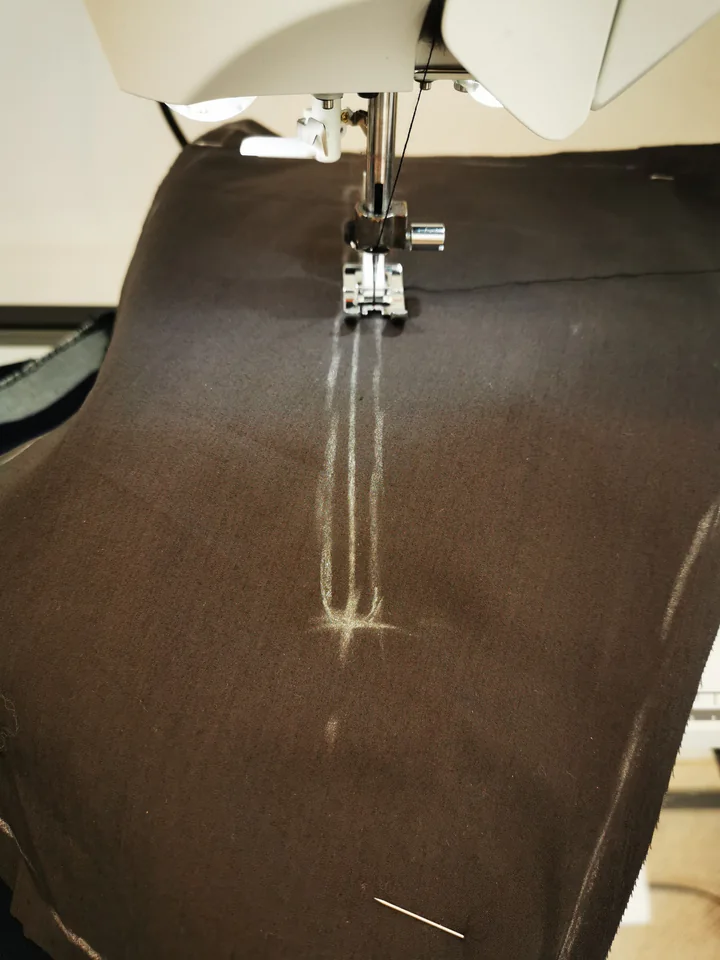 Sewing machine stitching the rounded opening outline through brown lining and navy trouser fabric.