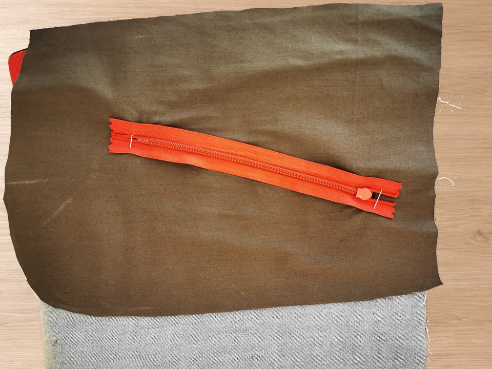 Reverse view of a red zipper pinned over brown pocket lining behind the faced opening.