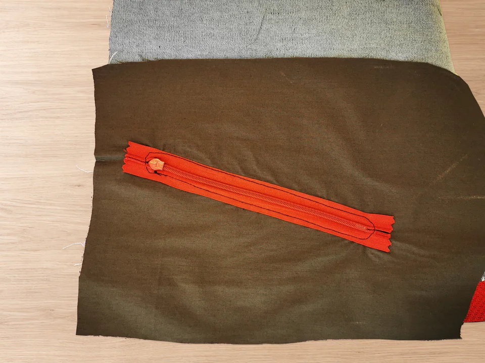Black stitching visible on both sides and ends of red zipper tape against brown pocket lining.