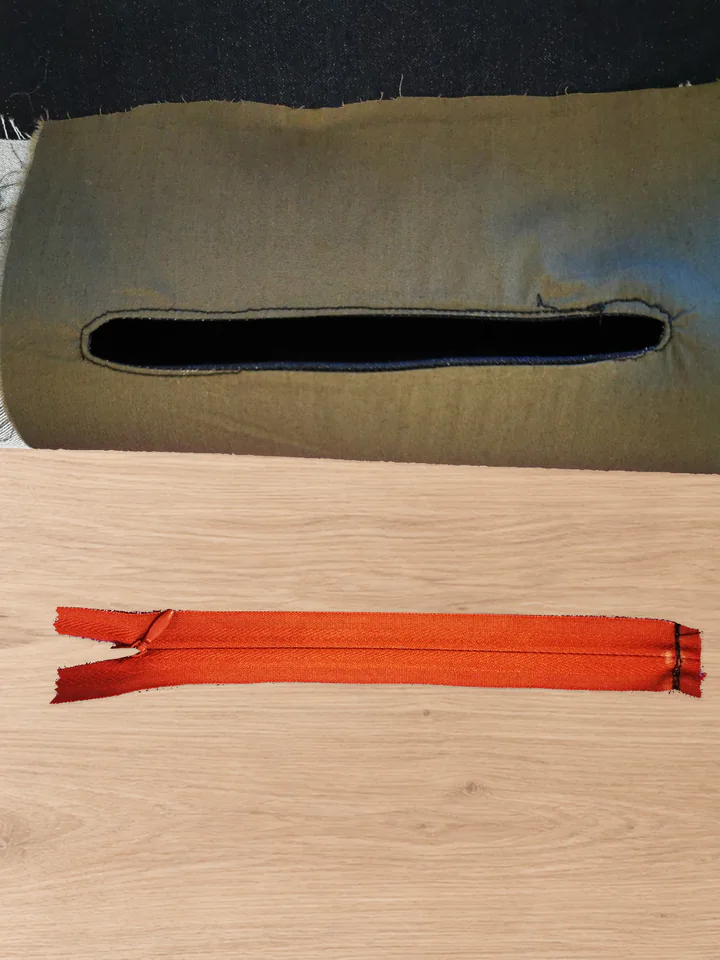 Brown back-pocket lining with its empty edgestitched opening and a separate red zipper laid below it.