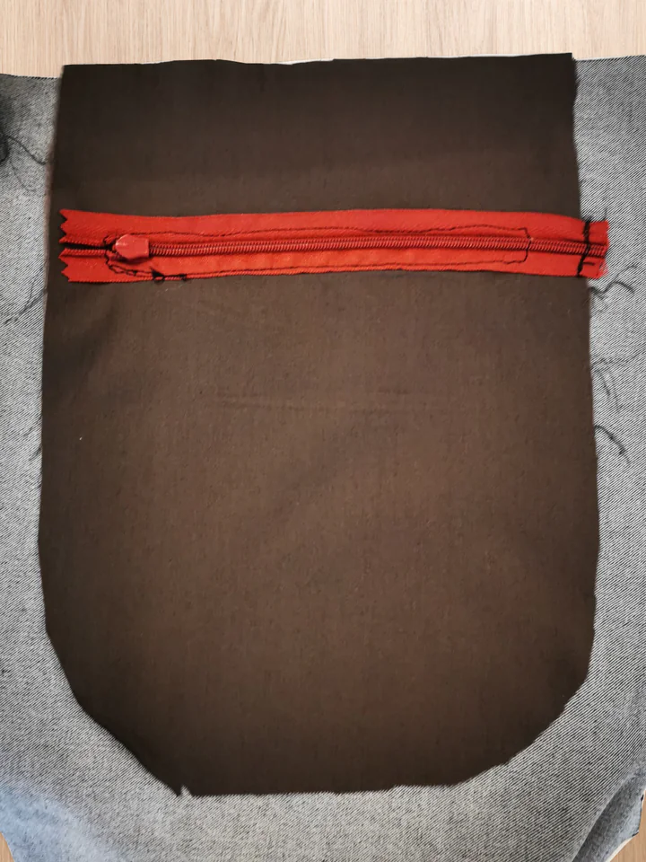 Reverse of the back-pocket opening with red zipper tape attached to the brown lining and the surrounding stitch line visible.