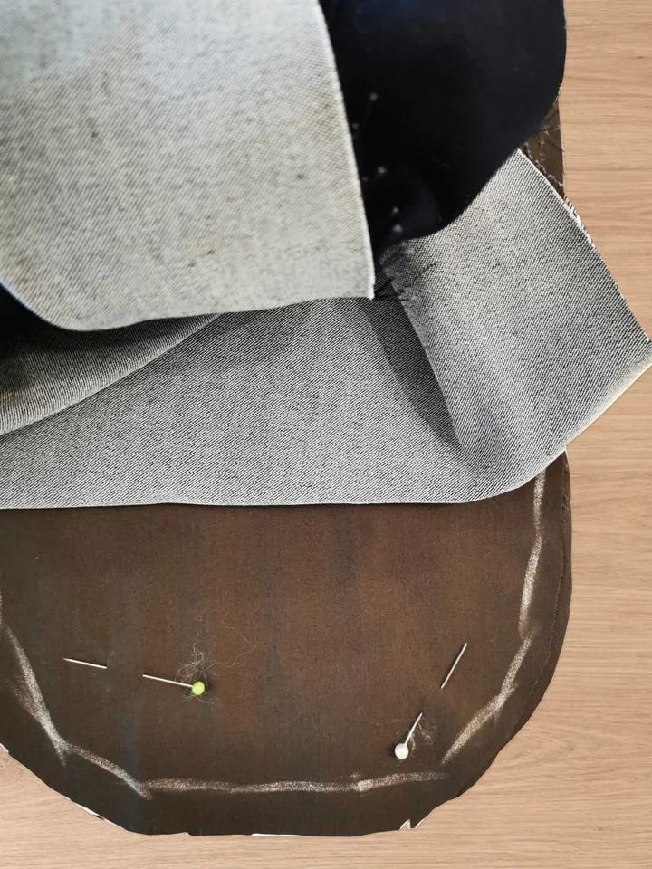 Brown pocket-bag layers pinned around their curved outline while the grey trouser fabric is folded away from the sewing area.