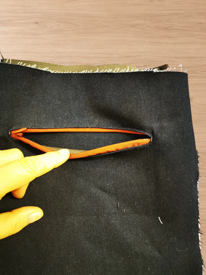 Finished red back-pocket zipper held open to reveal the navy main-fabric pocket facing inside the pocket.